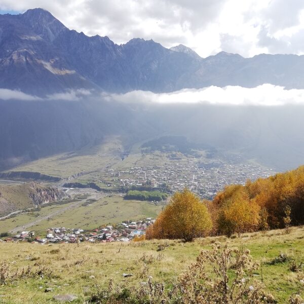 High angle view of Stepantsminda village in Kazbegi surrounded by huge mountains and autumn trees.