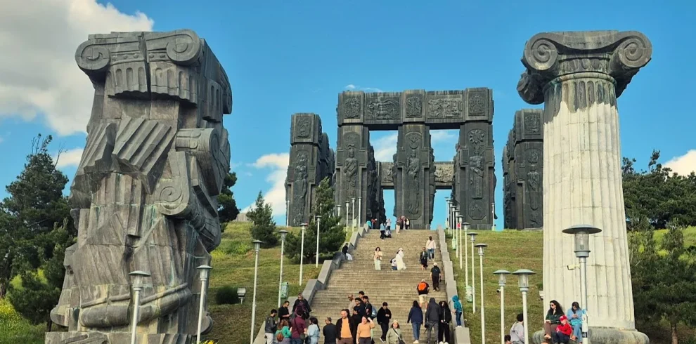 The Chronicle of Georgia monument on a sunny day with green hills and blue sky.