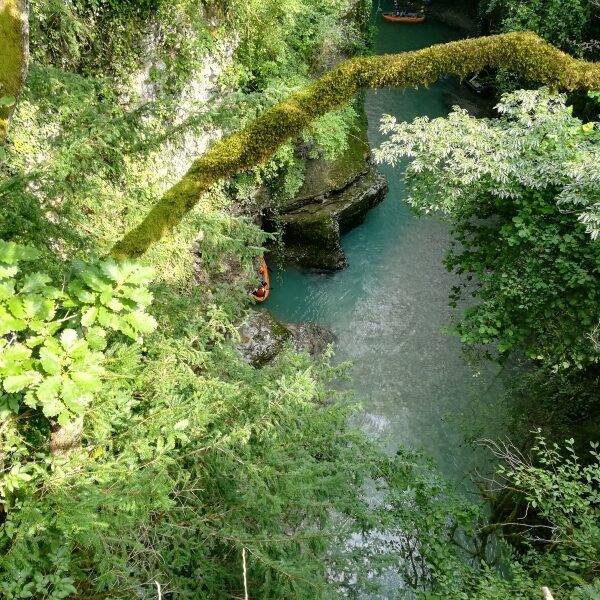 High angle view of Martvili Canyon with lush green forest and boats on the turquoise river.