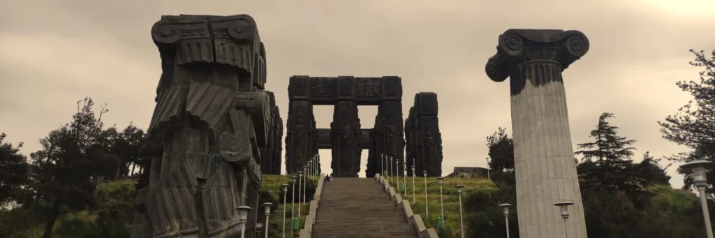 The monumental bronze and stone pillars of the Chronicle of Georgia under a dramatic sky