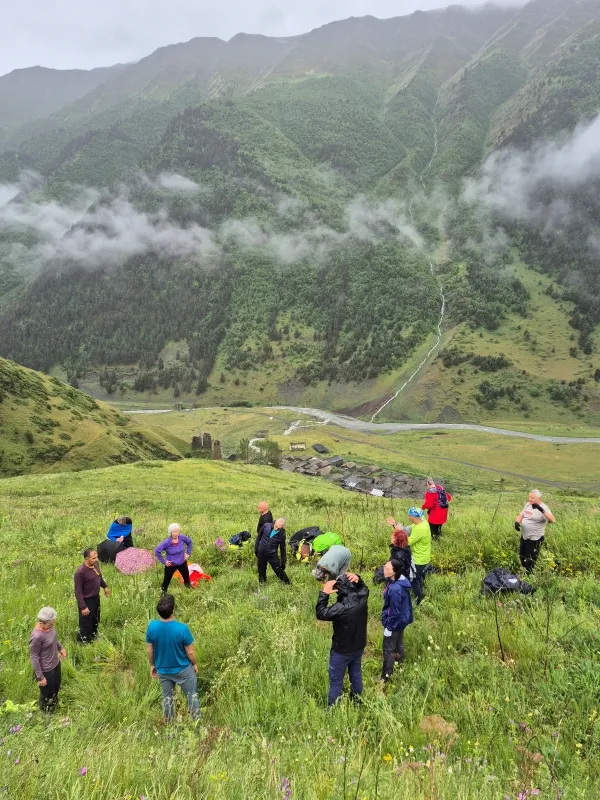 A group of hikers on a green mountain slope looking down at Dartlo village in the misty Pirikiti valley