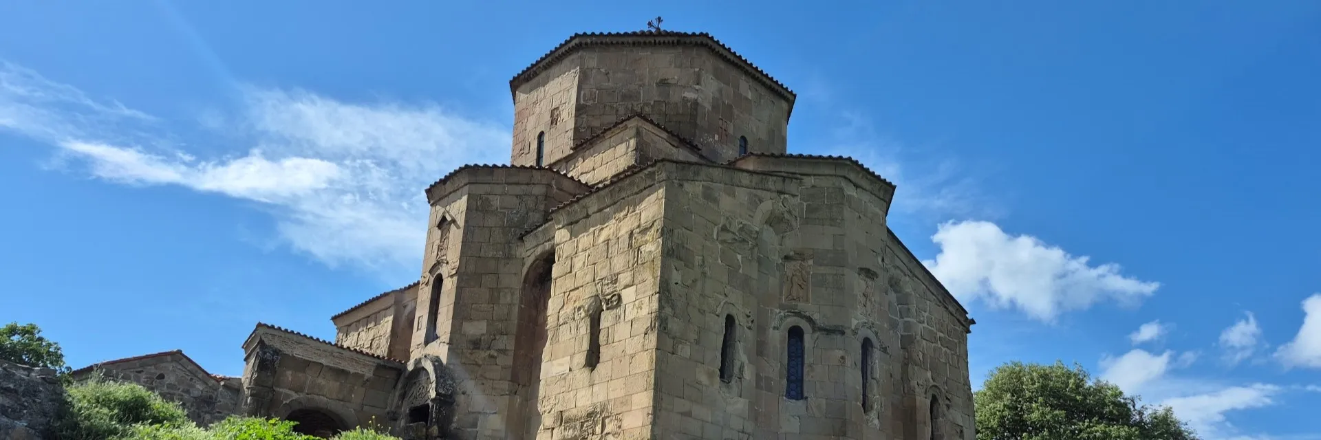 The ancient stone facade and dome of Jvari Monastery under a bright blue sky