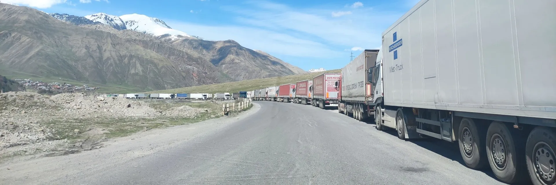 A long line of cargo trucks parked along the winding road near Jvari Pass in the Caucasus Mountains