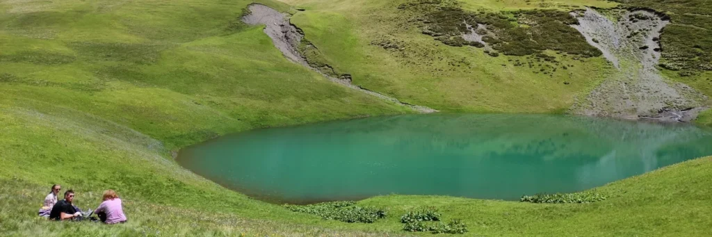 The crystal emerald waters of Oreti Lake in Tusheti with hikers resting on the green shore