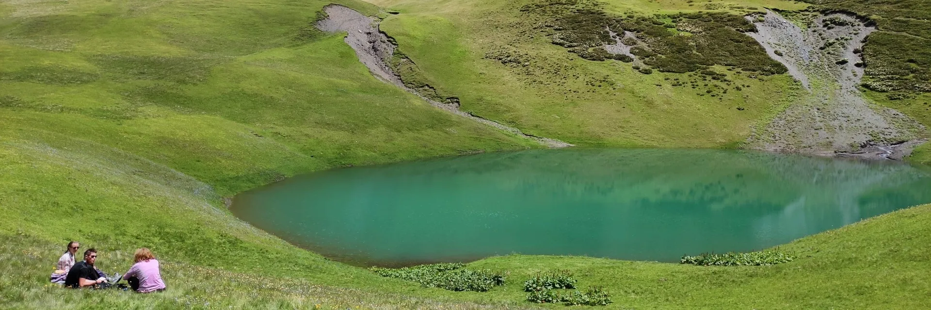 The crystal emerald waters of Oreti Lake in Tusheti with hikers resting on the green shore