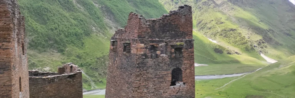 Ruins of medieval stone fortress towers in Tusheti looking over a green mountain river valley