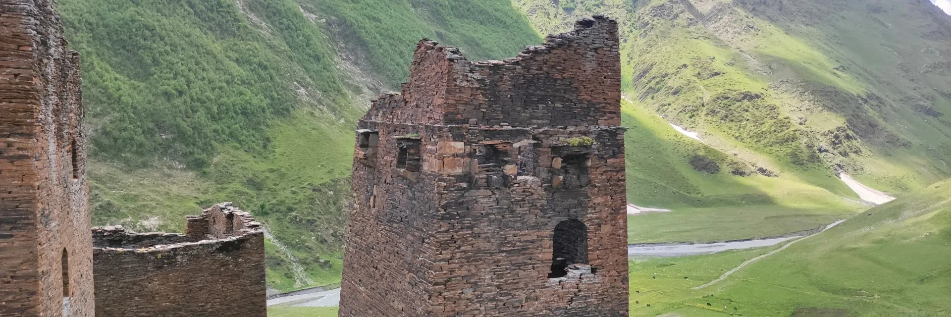 Ruins of medieval stone fortress towers in Tusheti looking over a green mountain river valley